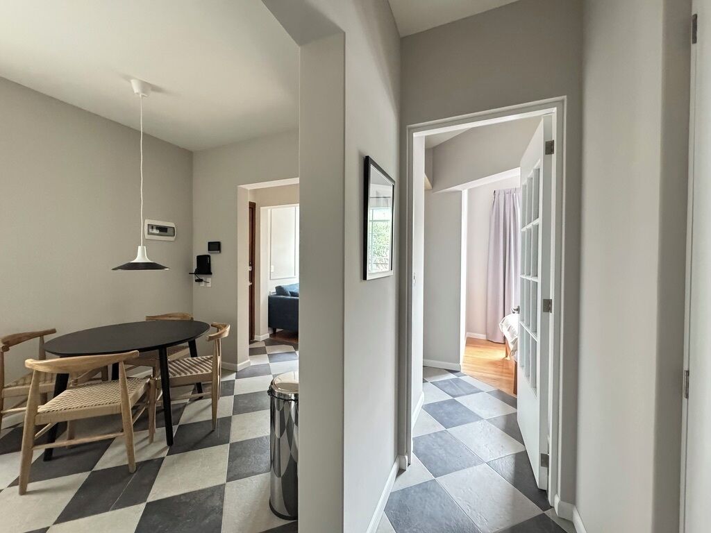 A dining area with a table and chairs, a checkered floor, and a hallway leading to another room.