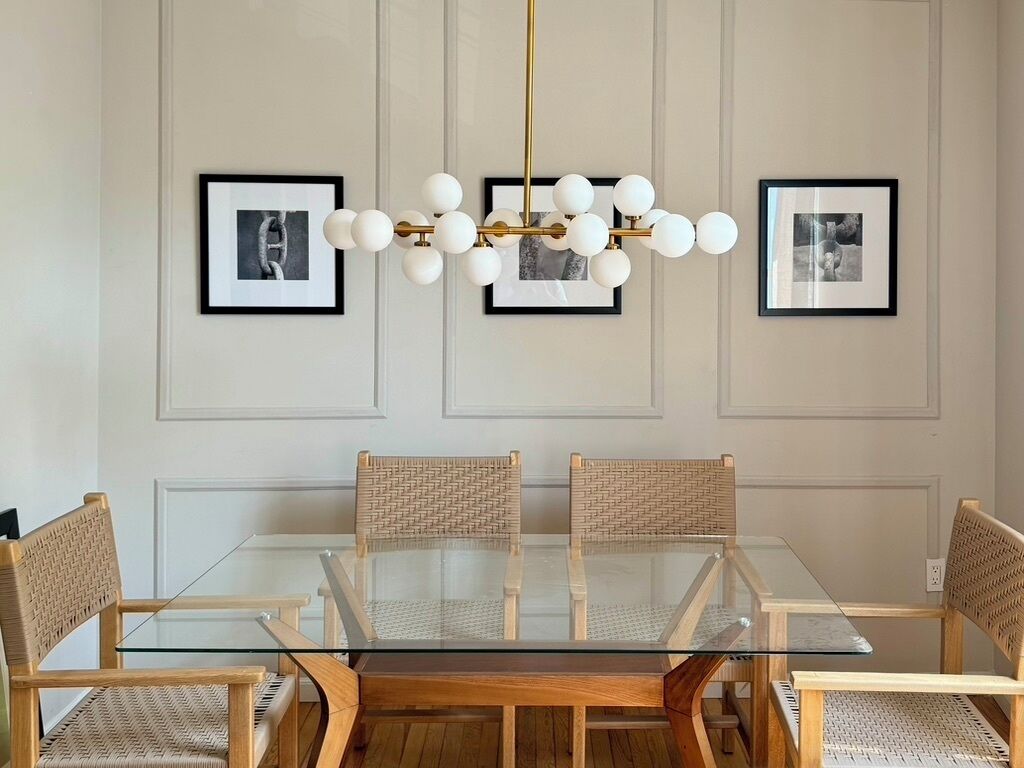 Uma área de refeições com mesa de vidro, cadeiras de vime e um candelabro.