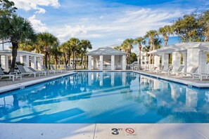 A swimming pool with lounge chairs and a covered pavilion, surrounded by palm trees.