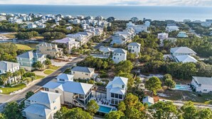 A coastal residential area with houses featuring modern architecture, a central road, and a visible swimming pool.