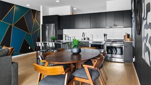 Una cocina moderna con armarios oscuros, un refrigerador de acero inoxidable y una zona de comedor con una mesa redonda de madera y sillas.