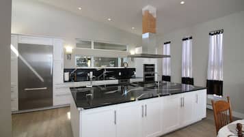A modern kitchen with white cabinetry, a stainless steel refrigerator, a black countertop, and a large island.