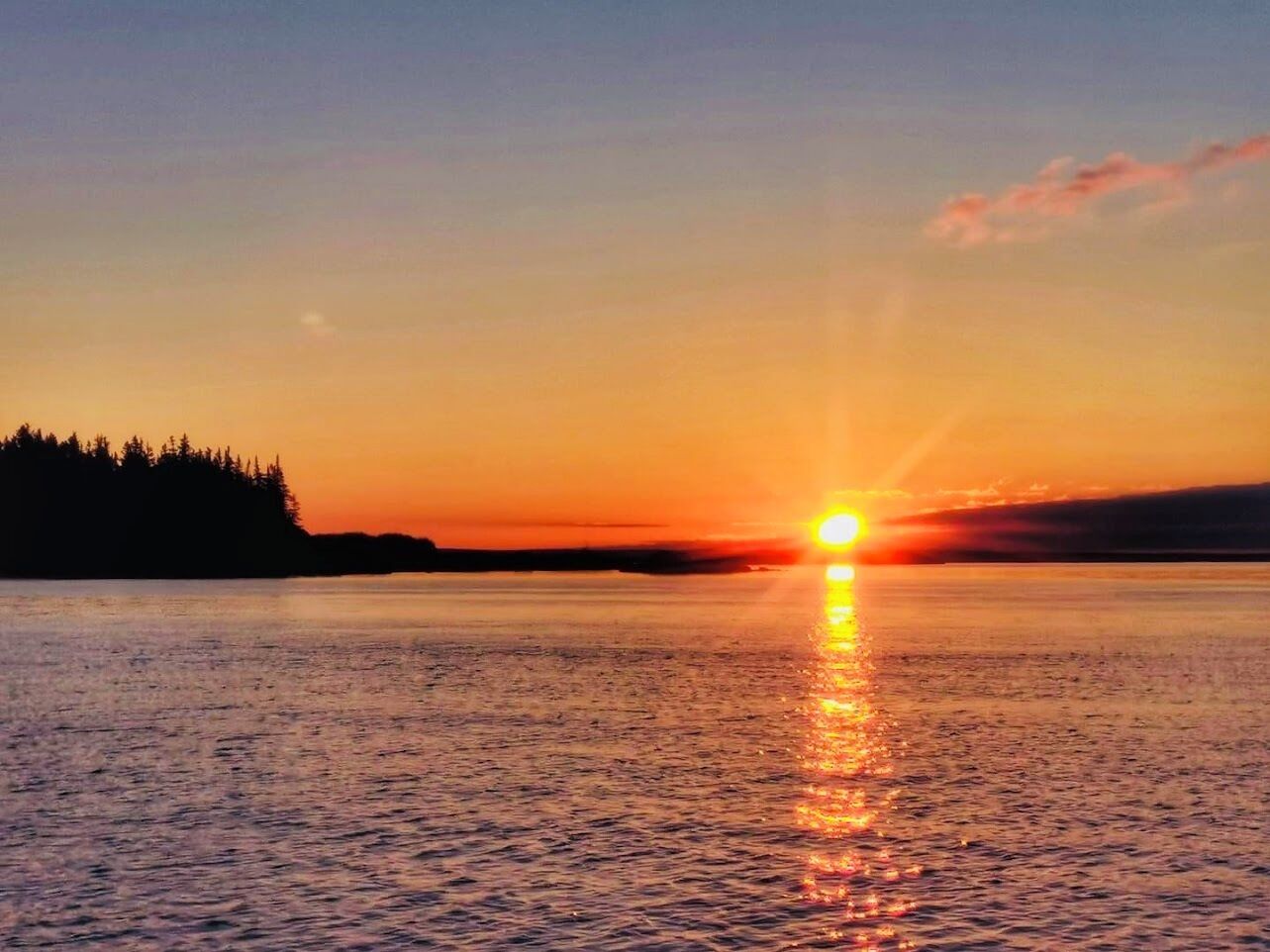 A sunset over a calm body of water with a forested shoreline.