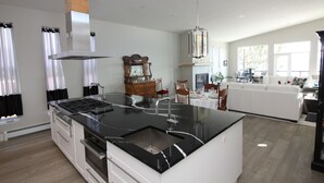 Et moderne køkken med en central ø, rustfrie stålapparater og et spiseområde med en hvid sofa og bord.