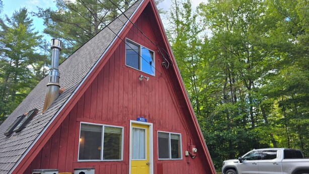 A red cabin with a yellow door, a chimney, and propane tanks. - Cozy 2-bedroom chalet in lovely Carrabassett Valley (Carrabassett Valley)