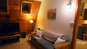 A cozy living room with a wooden wall, a television, a sofa, and a lamp. - Cozy 2-bedroom chalet in lovely Carrabassett Valley (Carrabassett Valley)