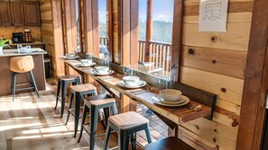A wooden interior with a long dining table set for four, bar stools, and a kitchen area visible in the background. - 6BR Sleeps 24 Smoky Mountain Retreat w/ Private Indoor Pool + Game Room (Sevierville)