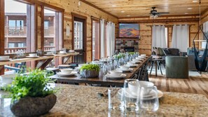 A long dining table set with plates, glasses, and a potted plant, wooden walls, and a large window with a view. - 6BR Sleeps 24 Smoky Mountain Retreat w/ Private Indoor Pool + Game Room (Sevierville)