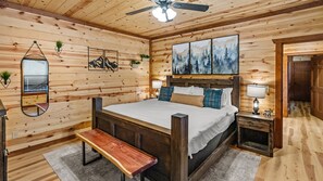 A wooden-paneled room with a bed, a bench, a nightstand, a mirror, and artwork on the walls. - 6BR Sleeps 24 Smoky Mountain Retreat w/ Private Indoor Pool + Game Room (Sevierville)