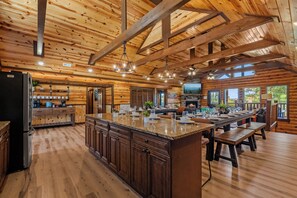 A spacious kitchen with a large island, wooden beams, and a stone fireplace. - 8BR Luxury Lodge w/ Indoor Pool, Hot Tub & Mountain Views, Sleeps 28 (Sevierville)