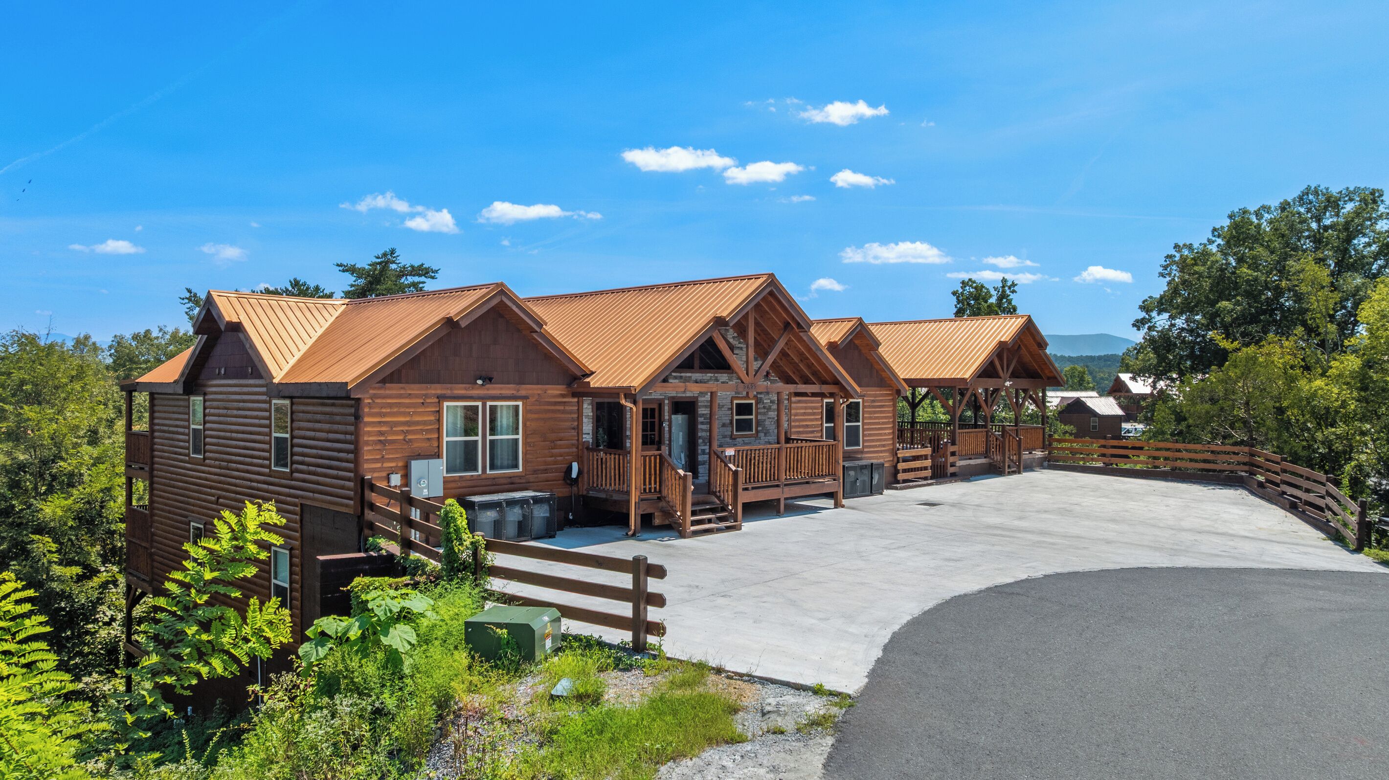 A row of wooden cabins with a covered outdoor area, surrounded by greenery and a clear sky.