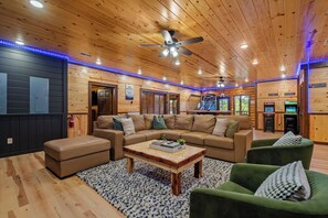 A cozy living room with a sectional sofa, a coffee table, and a green armchair. - 8BR Luxury Lodge w/ Indoor Pool, Hot Tub & Mountain Views, Sleeps 28 (Sevierville)