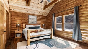Een slaapkamer in een houten chalet, met een bed, bedlampen, een raam en een plafondventilator.