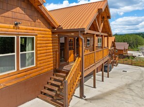 A wooden log cabin with a balcony and a staircase leading to the entrance. - 8BR Mountain Escape w/ Indoor Pool + Mins to Parkway (Sevierville)