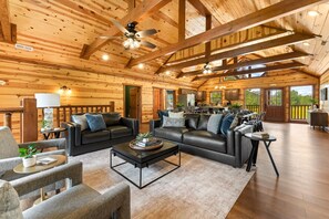 A spacious log cabin interior with a living area featuring a black leather sofa, a coffee table, and a fireplace. - 8BR Mountain Escape w/ Indoor Pool + Mins to Parkway (Sevierville)