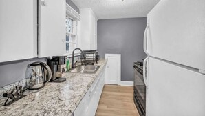 A compact kitchen with white cabinets, a granite countertop, a built-in oven, and a window with white blinds. - Weber Duplex House Upper Unit Near Highland Square (Akron)