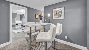 A modern dining area with a glass-top table, white chairs, and a pendant light. - Weber Duplex House Upper Unit Near Highland Square (Akron)