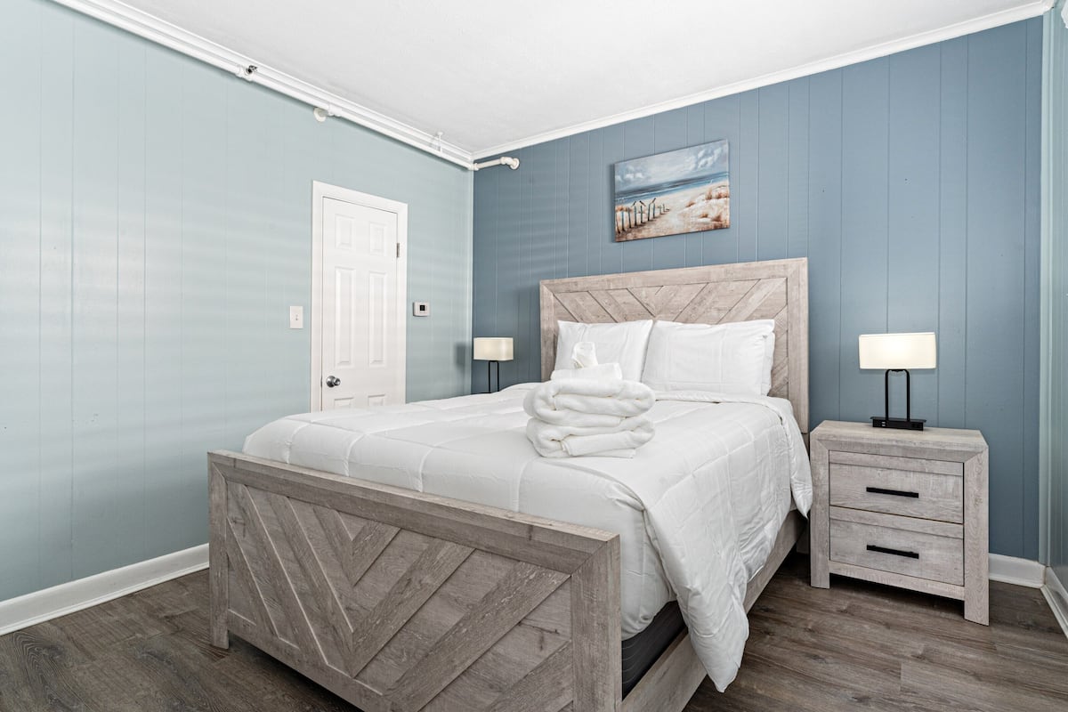 A bedroom with a bed, nightstands, a door, and a wall painting.