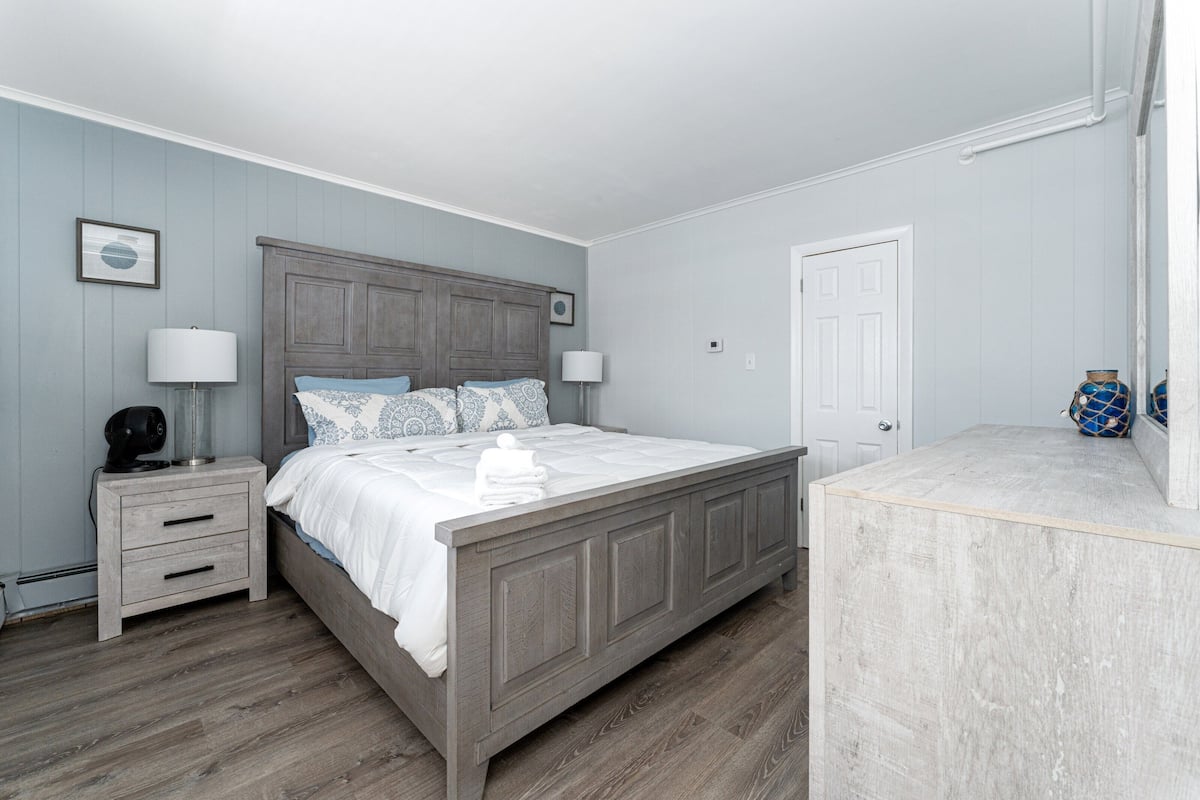 A bedroom with a wooden bed, two bedside tables, a nightstand, a white door, and a small decorative item on the nightstand.