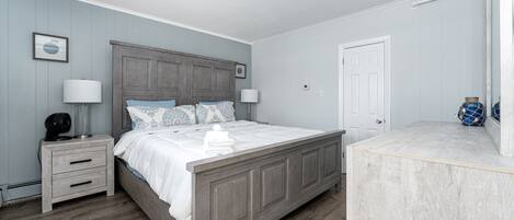 A bedroom with a wooden bed, two bedside tables, a nightstand, a white door, and a small decorative item on the nightstand.