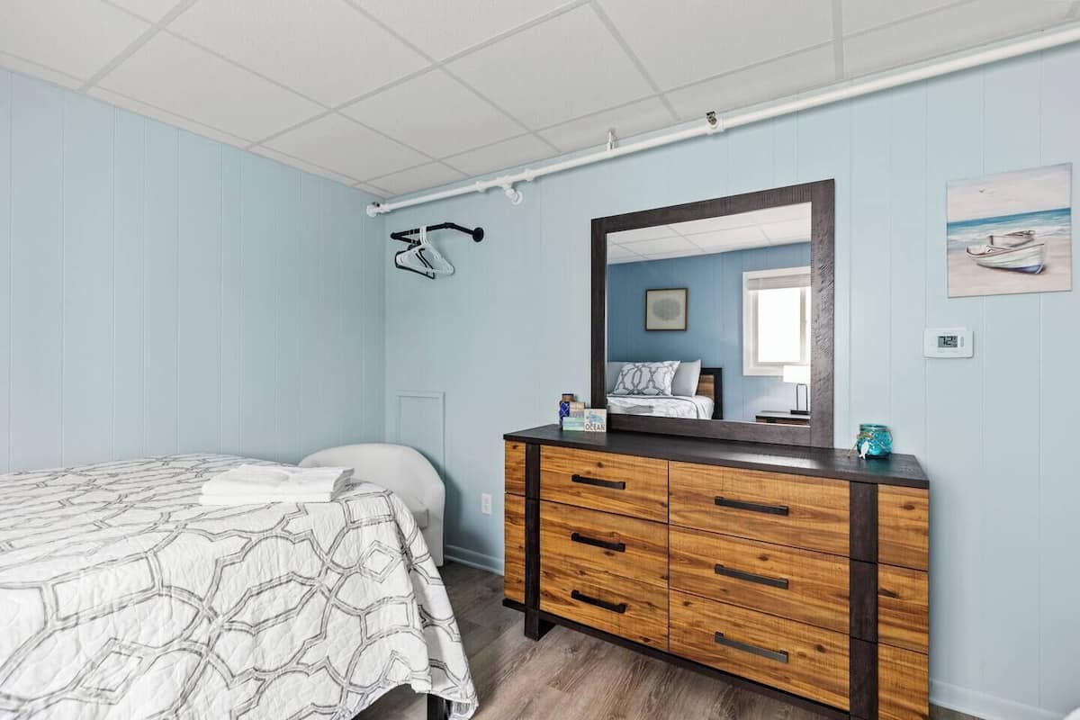 A bedroom with a bed, a wooden dresser, a mirror, and a wall-mounted bicycle rack.