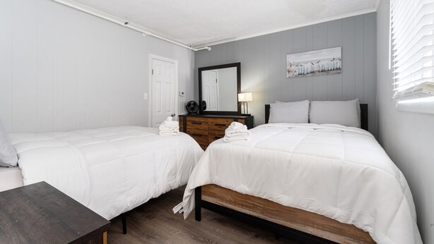 Une chambre d’hôtel avec deux lits simples, une commode en bois, un miroir et un tableau au mur.