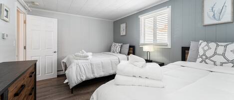 A bedroom with two beds, a dresser, a window with blinds, and a framed picture on the wall.