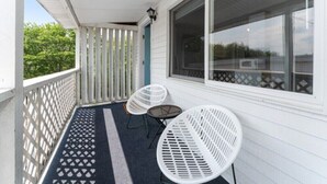 A covered porch with white railings, two white metal chairs, and a large window.
