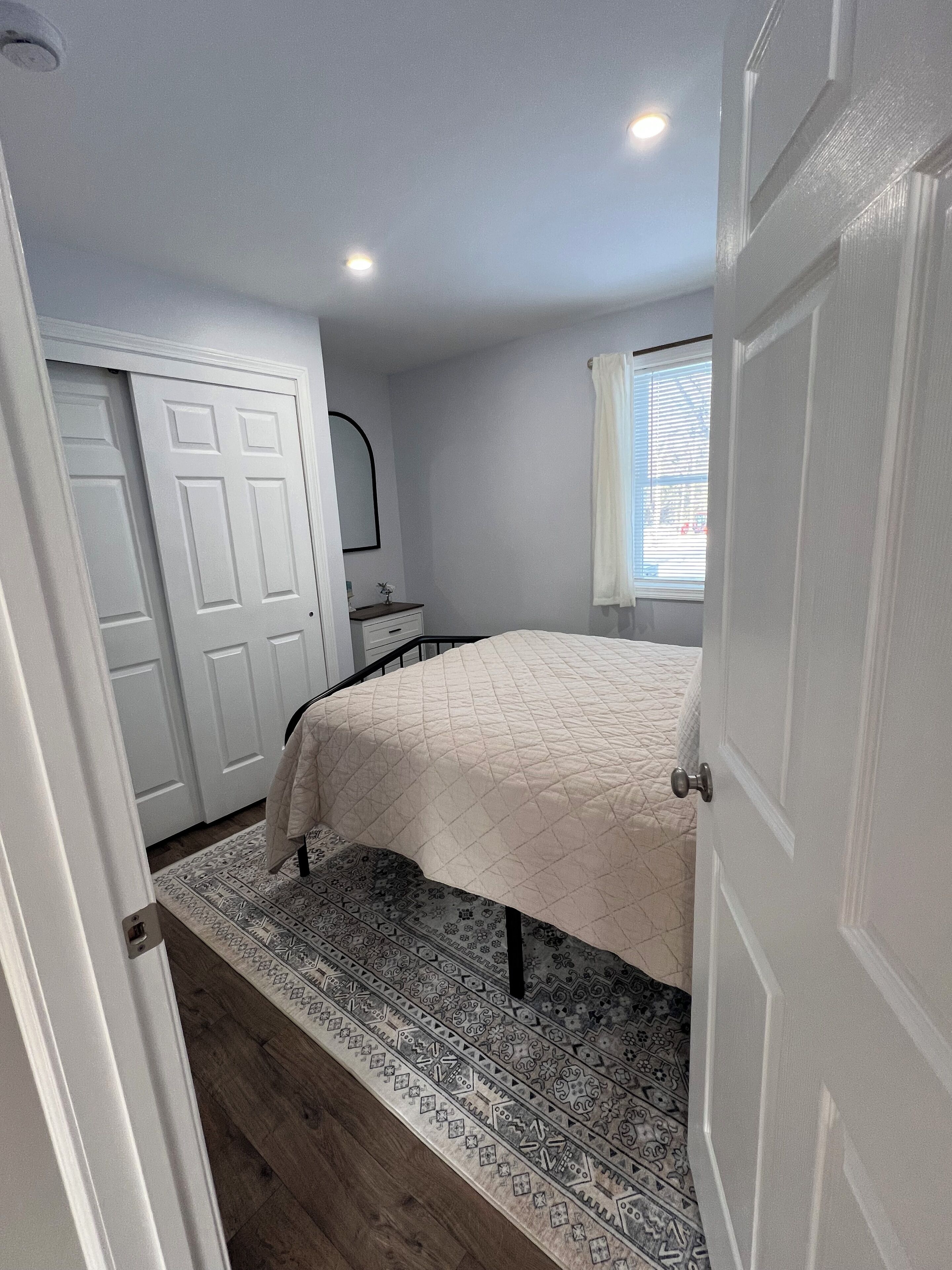 A bedroom with a bed, a nightstand, a dresser, a mirror, and a window with blinds.