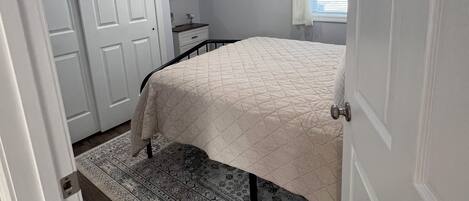 A bedroom with a bed, a nightstand, a dresser, a mirror, and a window with blinds.