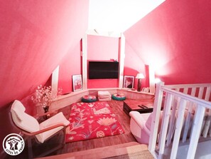 A cozy room with a red and white color scheme, featuring a sofa, a TV, and a small table. - Gîtes de France® - La Longère de Bessous (CONCORES)