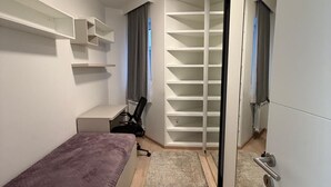 Een slaapkamer met een bed, een bureau, een stoel, een kledingkast en een inbouwplank.