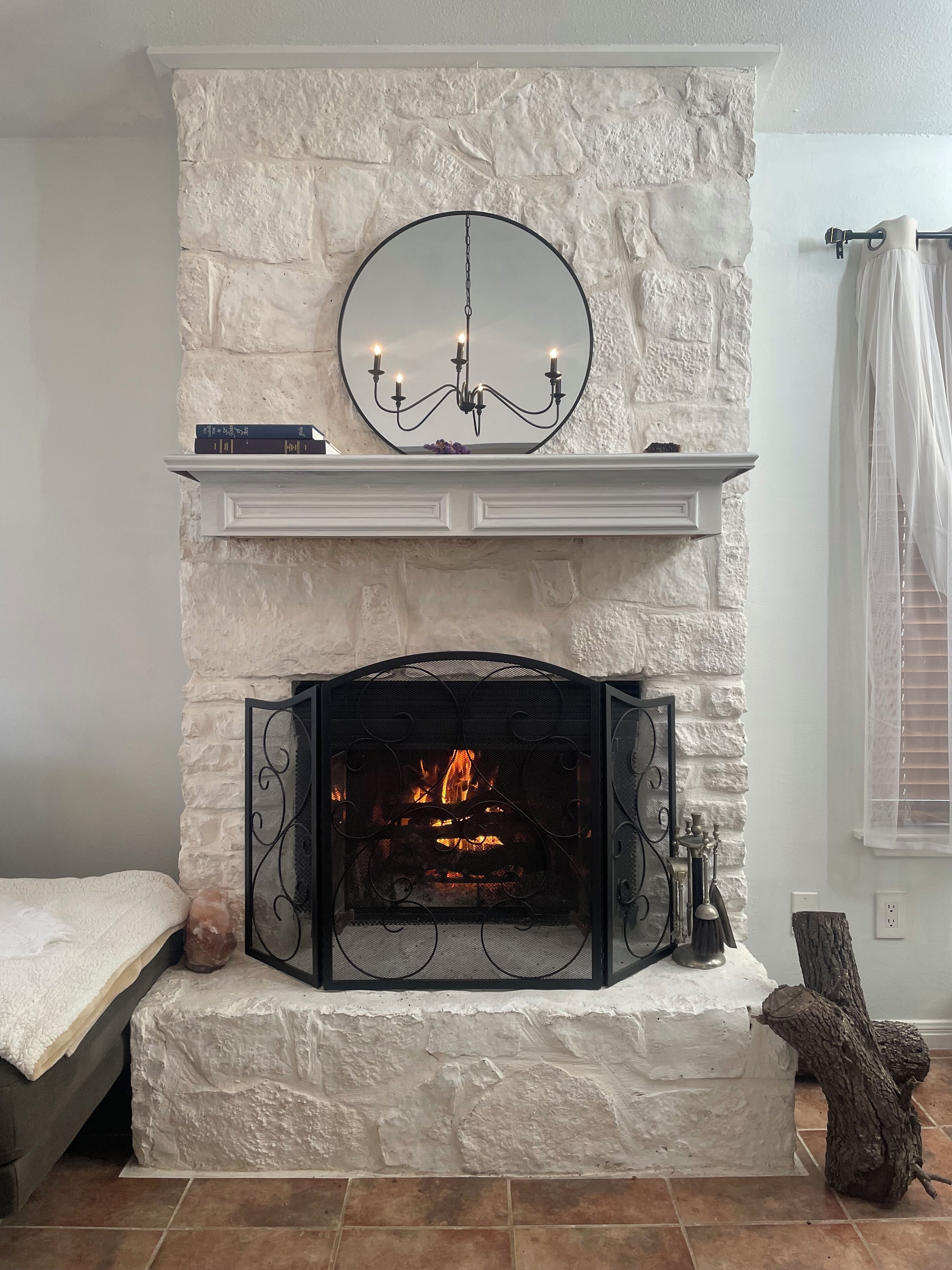 A fireplace with a stone wall, a mantel with books, and a hanging mirror.