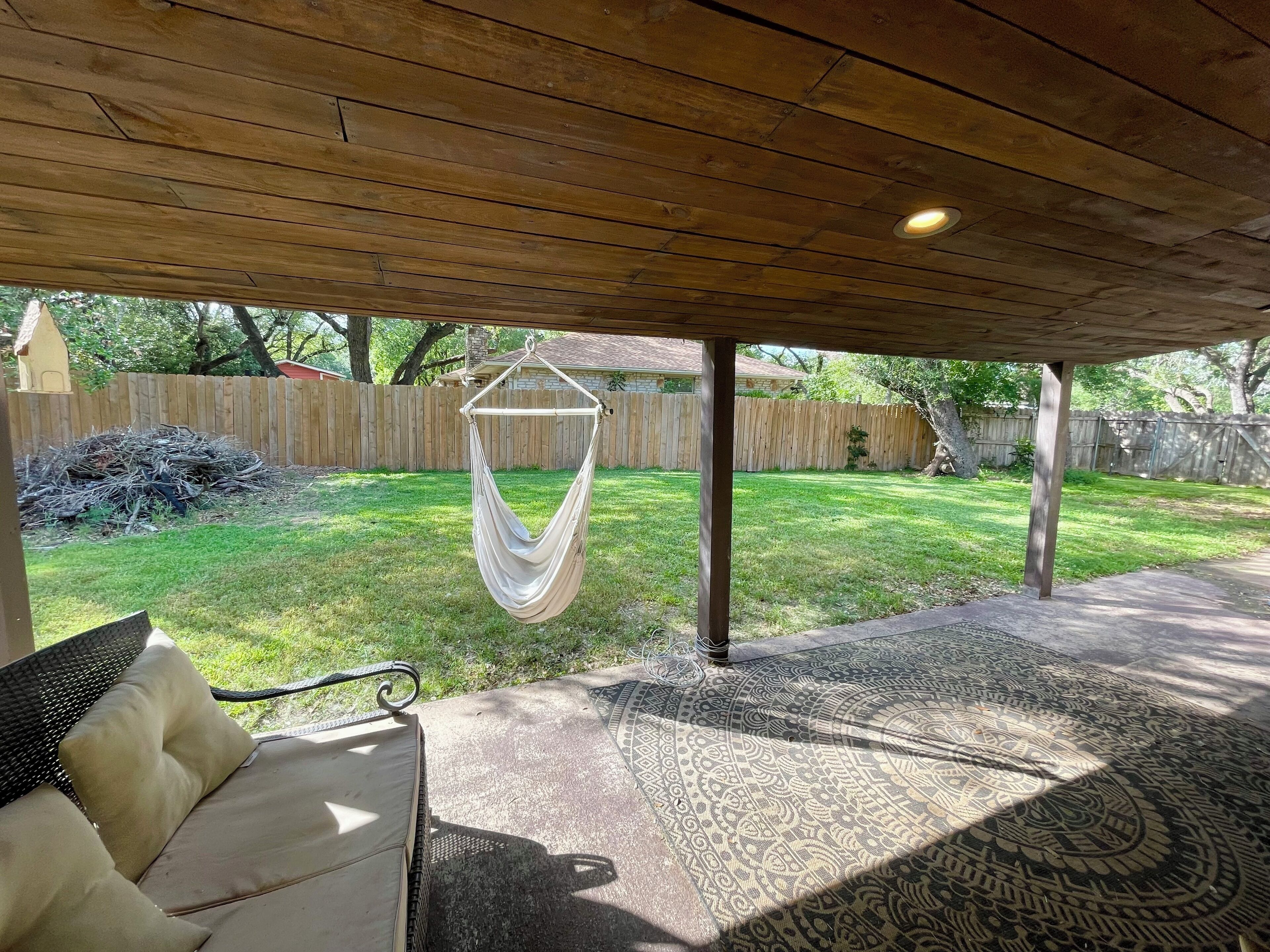 An outdoor patio area with a hammock, a patterned rug, and a cushioned seating area.