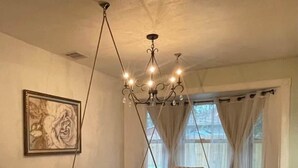 Une salle à manger avec une grande table, des chaises à motifs, un banc, un lustre et une œuvre d’art encadrée au mur.