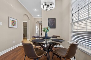 Dining area with a glass-top table, brown chairs, and bright window. - Central South Austin, Fenced Yard + Pets, Fire pit (Austin)