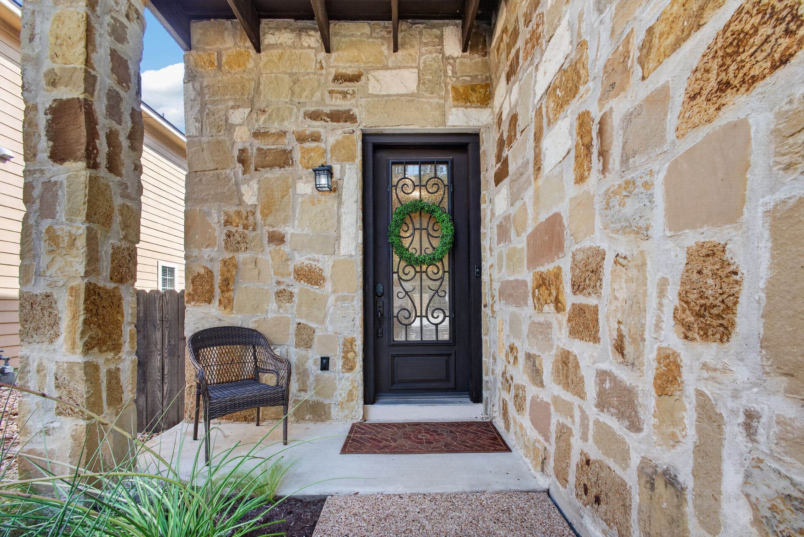A stone-clad front entryway features an ornate front door and a wicker armchair.