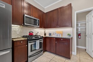 A kitchen with wooden cabinets, a stainless steel refrigerator, a microwave, a stove, and a tiled backsplash. - Central South Austin, Fenced Yard + Pets, Fire pit (Austin)