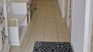 Um corredor estreito com uma cama de solteiro em metal, um penteou branco e um tapete estampado.
