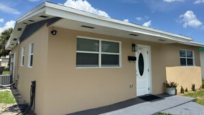 Una edificación de un solo piso con fachada color beige, una puerta blanca y un pequeño porche.