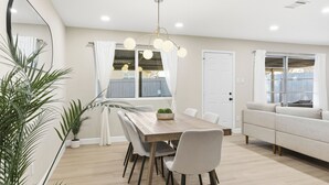 Een moderne eetruimte met een houten tafel, witte stoelen en een plafondlamp.