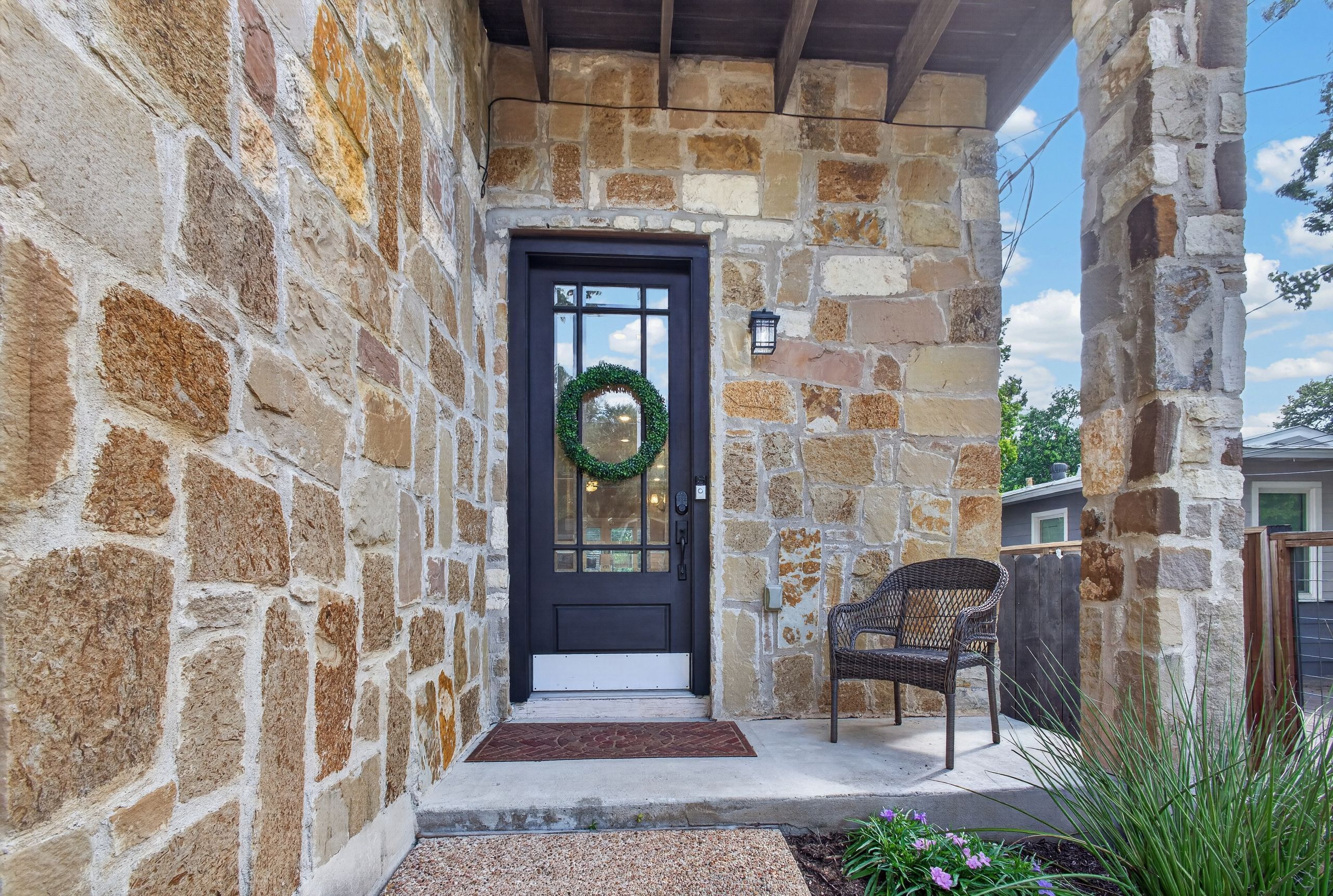 A stone building with a dark door, a wreath, and a wicker chair outside.