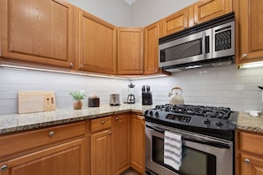 A kitchen with wooden cabinets, a stainless steel microwave, a gas stove, and a white tiled backsplash. - Dog-Friendly South Austin w/ Private Yard! (Austin)