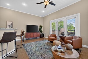 A living room with a ceiling fan, a flat-screen TV, a coffee table with decorative items, a patterned rug, and a seating area with two chairs and a sofa. - Dog-Friendly South Austin w/ Private Yard! (Austin)