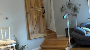 Une pièce avec une porte coulissante en bois, une chaise blanche, une petite plante, un canapé gris et un escalier.