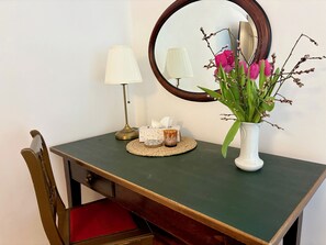 A small vanity table with a mirror, a lamp, a vase with flowers, and a tissue box.