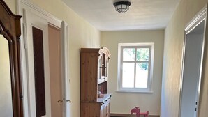 Un pasillo con piso de madera, un tapete rojo con diseño, un mueble de madera y una ventana que da a vistas de vegetación.