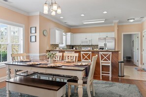 A modern kitchen with white cabinetry, a central island, and a dining area with a table set for four. - Family Oasis: Charming 3-BR Myrtle Beach Condo - Adventure, Sun & Golf Fun! (Myrtle Beach)
