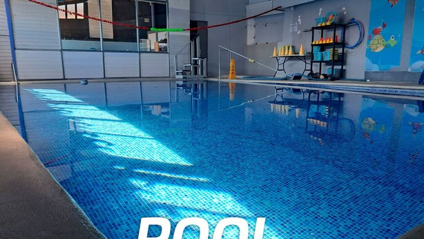 Una piscina interior con suelo de azulejos azules brillantes, una barrera de cuerda y un mural de criaturas marinas en la pared.