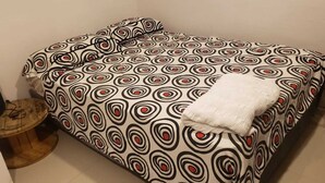 A bed with a patterned bedspread, a white blanket, and a small wooden stool with a cable. - Cabaña el Eden is an ideal place for family relaxation. (Santa Verónica)